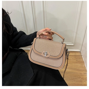 Detail of khaki woven saddle bag featuring a round metal ring clasp and top handle grip