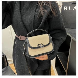 Detail of straw and black leather saddle bag featuring a refined dual-ring metal buckle