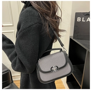 Close-up of black and white striped crossbody saddle bag with a silver round metal lock