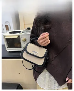 Détail du sac selle montrant le tissu beige, le cuir noir et le logo argenté