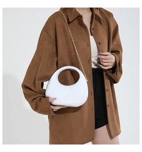Chic white acrylic crescent box bag with gold chain strap held by a model in brown