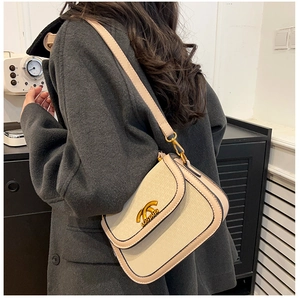 Detail of beige saddle bag with black trim and gold logo worn on shoulder