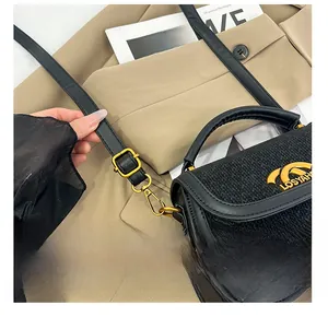 Detail of black leather saddle bag with woven texture, gold logo and adjustable strap