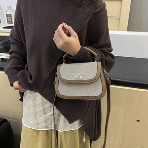 Sac selle rétro en tweed avec bordure en cuir marron et fermoir métallique tenu par un mannequin