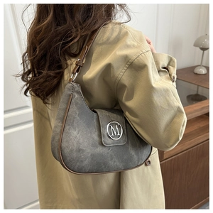 Detail of grey crescent underarm bag with silver M logo and brown trim on a trench coat