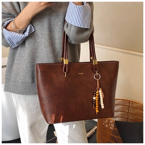 Détail du sac cabas marron vintage avec texture cuir et breloque à pompons bohème