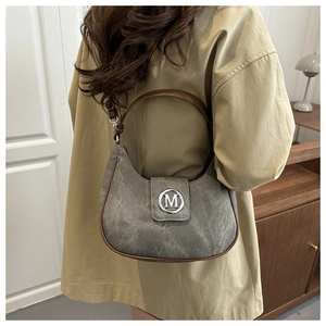 Detail of grey crescent bag with brown trim and metallic M-logo clasp on a shoulder strap