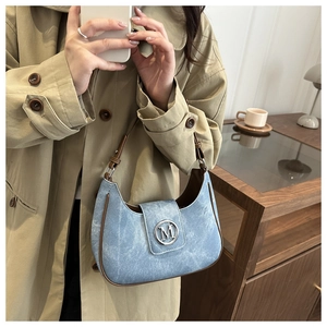 Close-up of a blue denim shoulder bag with brown leather trim and silver M logo