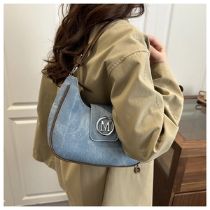 Detail of light blue crescent bag with brown leather trim and silver M-buckle on shoulder