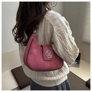 Detail of rose pink crescent bag with metallic M logo and brown trim worn by a model
