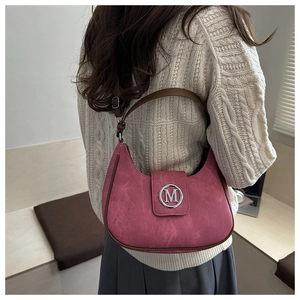 Detail of pink crescent bag with suede texture and metallic M buckle on shoulder