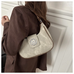 Detailed view of white crescent bag with silver M logo and brown trim worn with blazer