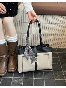 Detail of canvas tote bag with black leather trim, gold lock, and silk scarf on the handle