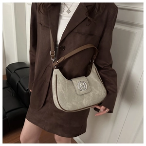 Detail of half-moon bag featuring textured beige fabric and brown leather trim accents