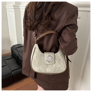 Detail showing retro hobo bag metal M logo and brown leather edge on a model shoulder