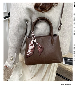 Detail of brown lychee leather handbag with decorative silk scarf and embossed logo