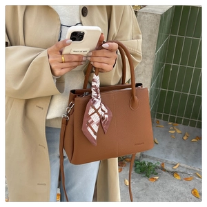 Close-up of brown lychee grain leather tote bag with decorative checkered silk scarf detail