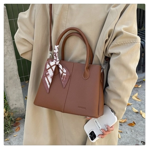 Brown leather tote bag with silk scarf detail worn by a model in a beige trench coat
