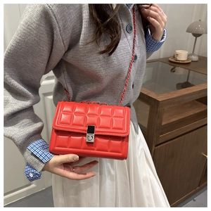 Detail of red quilted chain crossbody bag featuring silver metal lock and leather strap