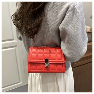 Detail of red quilted crossbody bag with silver metal clasp and chain strap on grey sweater