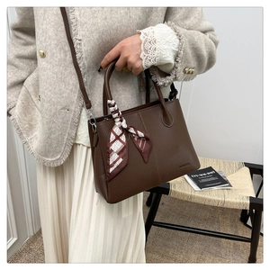 Detail of dark brown leather tote bag showing lychee grain texture and silk scarf handle