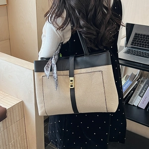Large beige canvas tote bag with black leather trim and decorative scarf shown on a model