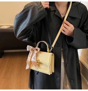 Detail of yellow leather crossbody bag with golden twist lock and decorative scarf on handle