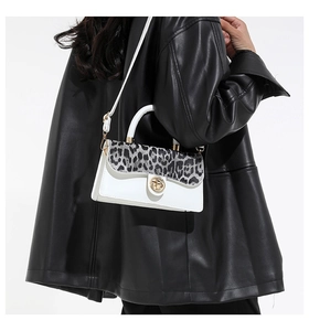 Detail of white and leopard print crossbody bag with gold twist lock on black leather jacket