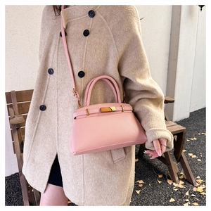 Detail der rosa Lederhandtasche mit Goldbeschlag an einem Model im beigen Mantel