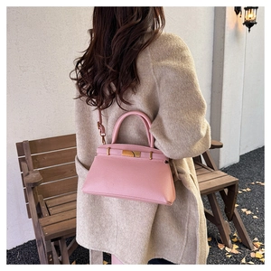 Details einer rosa Kelly-Handtasche mit goldenem Schloss und Lederstruktur auf einer Holzbank