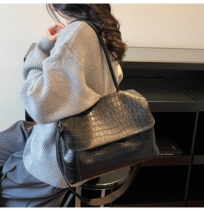Side view of a black crocodile texture shoulder bag worn with a gray knit sweater