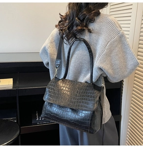 Detail showing black crocodile pattern leather texture on a large flap shoulder bag