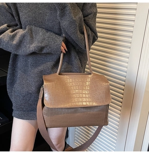 Detail of brown crocodile textured tote bag with wide strap and sleek flap closure