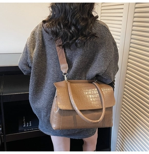 Close-up of brown crocodile pattern handbag with wide woven strap for commute