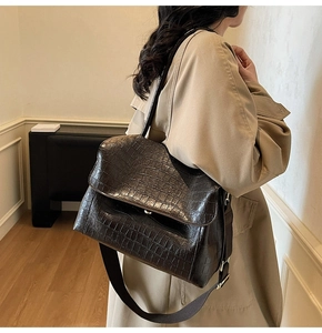 Deep brown oversized shoulder bag with croc-embossed texture worn with a trench coat