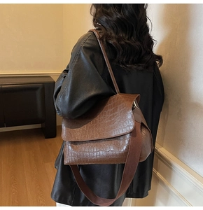 Detail of dark brown croc-effect shoulder bag featuring a wide fabric strap and flap closure