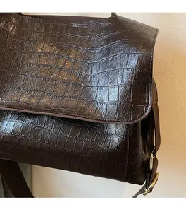 Detail of dark brown crocodile embossed leather bag with premium gold buckle