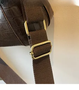 Detail of adjustable brown woven shoulder strap with gold metal buckle on tote bag