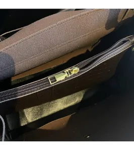 Macro shot of dark brown bag interior featuring a golden zipper and checkered leather trim
