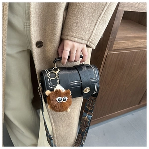Detail of a black faux leather cylinder handbag with retro wide strap and plush charm