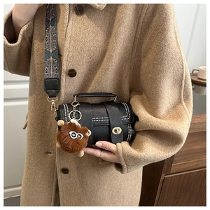 Detail view of black vintage leather handbag with wide embroidered strap and plush charm