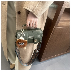 Detail of dark green vintage handbag with wide floral strap and cute plush bear charm