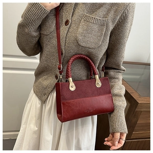 Detail of burgundy crossbody bag with mixed textures and woven handle craftsmanship