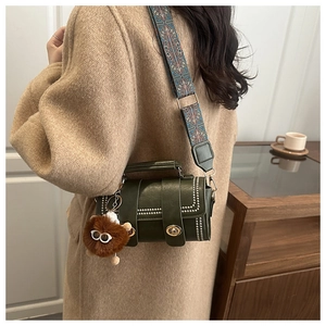 Detail of dark green vintage handbag with rivet decor, ethnic strap and plush charm