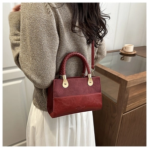 Detail of red crossbody bag featuring matte contrast panel and woven handle in warm home setting