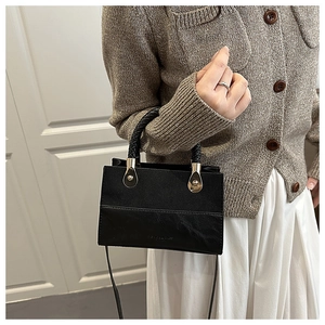 Detail of black textured PU leather handbag with gold hardware and woven handle worn by model