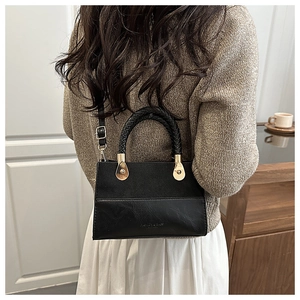 Detail of black faux leather handbag featuring woven handle and gold hardware on model