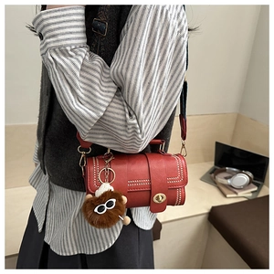 Detail of red leather crossbody bag with white studs, gold lock and pom-pom charm
