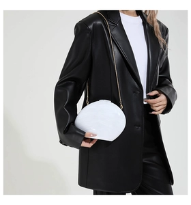 Schicke weiße Marmor-Acryl-Clutch mit goldener Kette auf schwarzem Lederblazer gezeigt
