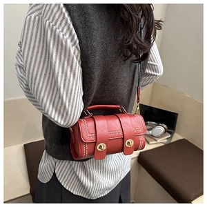 Detail of red cylindrical handbag with wide strap and twin turn-lock closures